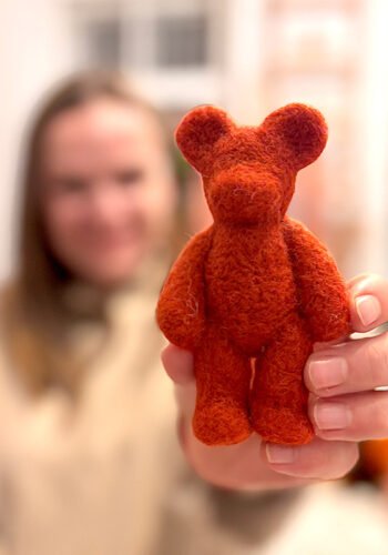 Raudonas veltas meškiukas iš vilnos, laikomas rankoje